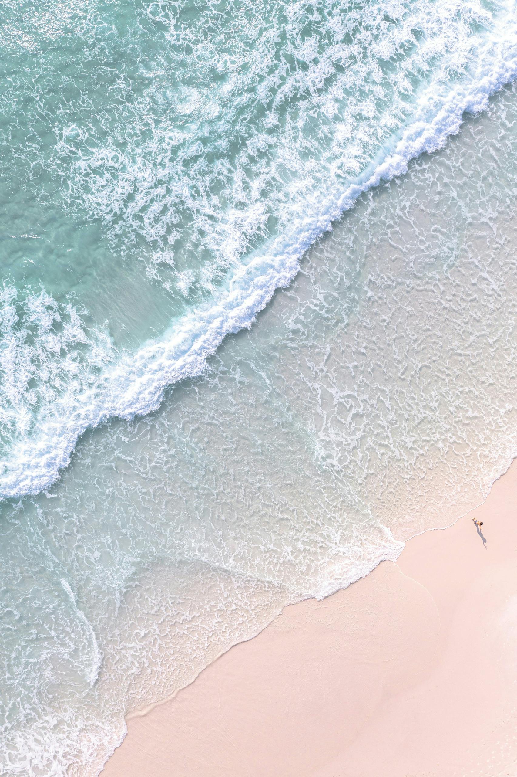 Stunning aerial shot of waves crashing on a tranquil sandy beach.